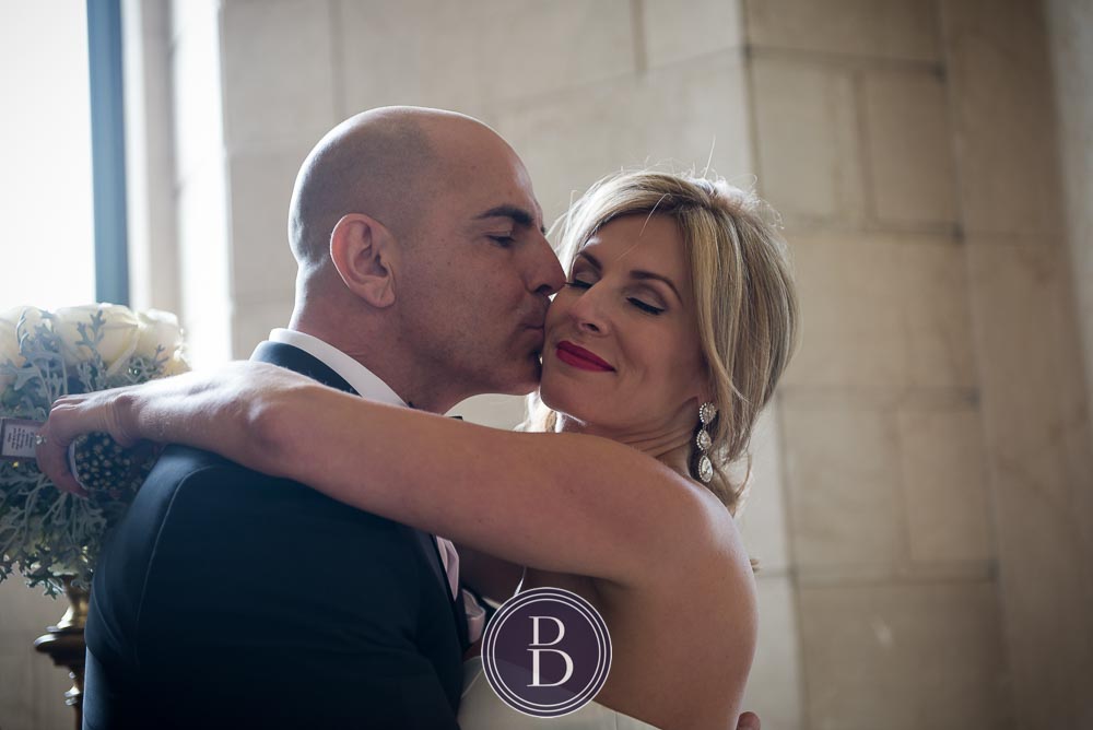 An elegant blue winter wedding. Bride and groom hugs and kisses at Hamilton building in Winnipeg