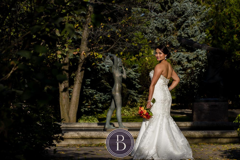 Winnipeg wedding photos bride looking back with a bouquet at Assiniboine Park Leo Mol Garden