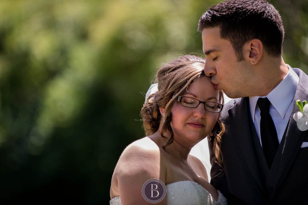 Groom kissing his bride formal photos on wedding day Manitoba legislative grounds in summer