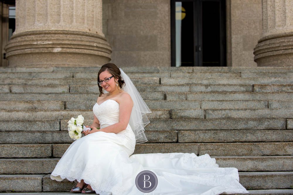 Bride sitting on stairs during formal portrait Manitoba Legislative building