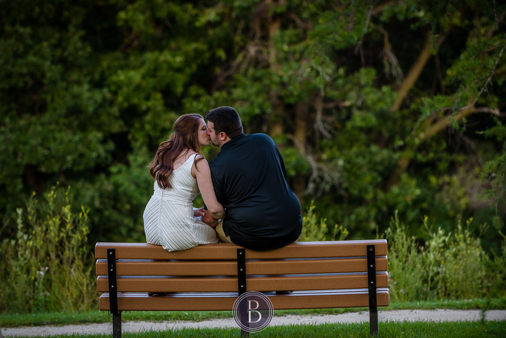 engaed couple kiss sittin on a bench at park